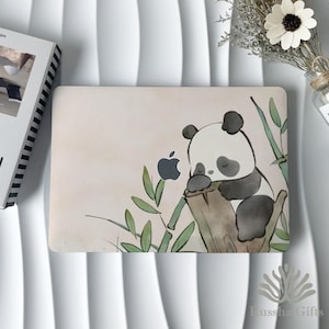 Może przedstawiać: Etui na laptopa z akwarelową ilustracją śpiącej pandy. Panda jest czarno-biała, spoczywa na pniu drzewa z łodygami bambusa. Widoczne jest logo Apple. Etui ma jasnobeżowe tło.