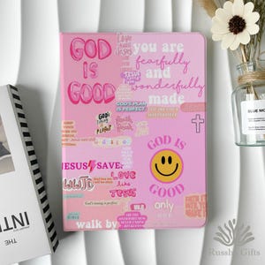 May include: Pink tablet case with the words "GOD IS GOOD" and other inspirational phrases in various fonts. A yellow smiley face is also featured. The case is decorated with a cross and other religious symbols.