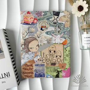 May include: A rectangular notebook cover featuring a collage of various stickers and paper cutouts, including a strawberry cake, Miffy, a die, a bear face, and Japanese postage stamps. The design incorporates floral patterns, cartoon characters, and text.