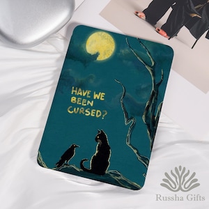 May include: A rectangular teal-colored decorative item with a spooky illustration. It features a black cat and raven under a full moon, with the text "HAVE WE BEEN CURSED?" in gold lettering. A dark tree silhouette adds to the eerie scene.