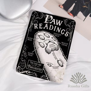 May include: A black and white rectangular sign featuring the words "PAW READINGS" and a cat paw illustration. The sign also includes the text "The Lost Art of Pawlmistry" and various labeled paw features.