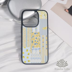 May include: A phone case with a patchwork design featuring lemons, blueberries, and stripes in yellow and blue. The case has a black border and a cutout for the camera. The design includes a variety of patterns and fruit illustrations.