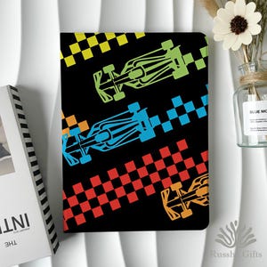 Peut inclure: Un carnet rectangulaire à couverture noire orné de trois voitures de course stylisées en vert citron, bleu vif et orange. Chaque voiture est accompagnée d'un motif de drapeau à damier assorti disposé en bandes diagonales sur la couverture.