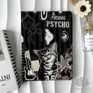 May include: A rectangular notebook cover featuring a black and white collage design with a spider, a melting clock, a single eye, a guitar, a cat, and a star. The text A FUCKING PSYCHO is printed in bold white letters against a black striped background.
