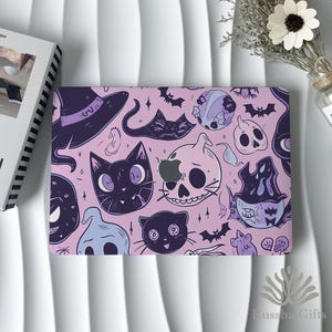 May include: A laptop case featuring a pink backdrop with a repeating pattern of Halloween-themed illustrations. The design includes black cats, witch hats, bats, skulls, and ghosts in purple, black, and light blue.