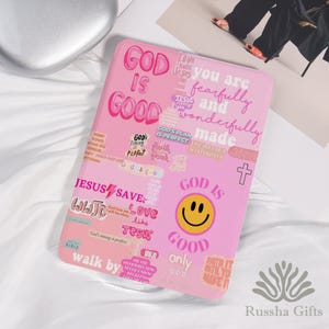 May include: Pink tablet case with the words "GOD IS GOOD" and other inspirational phrases in various fonts and colors. Features a smiley face and a cross. The case is decorated with stickers and the text "JESUS SAVE".