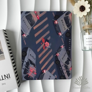 May include: A dark blue notebook cover featuring a whimsical illustration of a person on a crosswalk surrounded by police cars. The police cars have flashing red and white lights. The word "POLICE" is visible on the cars. The notebook is a unique gift.