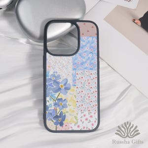 May include: A black phone case with a patchwork design featuring floral patterns in blue, pink, and white. The case has a dark border and a cutout for the camera. The design includes a variety of flower illustrations.
