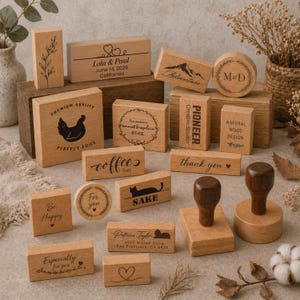 Könnte beinhalten: Eine Sammlung von Holzstempeln mit verschiedenen Designs und Texten. Einige Stempel zeigen Sätze wie "Danke", "Coffee Time" und "Be Happy". Andere enthalten Illustrationen eines Berges, einer Katze und eines Huhns. Die Stempel sind aus hellem Holz gefertigt.