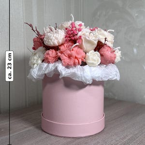 May include: A pink round gift box, approximately 8 inches in diameter and 9 inches tall, filled with a floral arrangement. The arrangement features white, pink, and red flowers, with a white paper ruffle around the base.