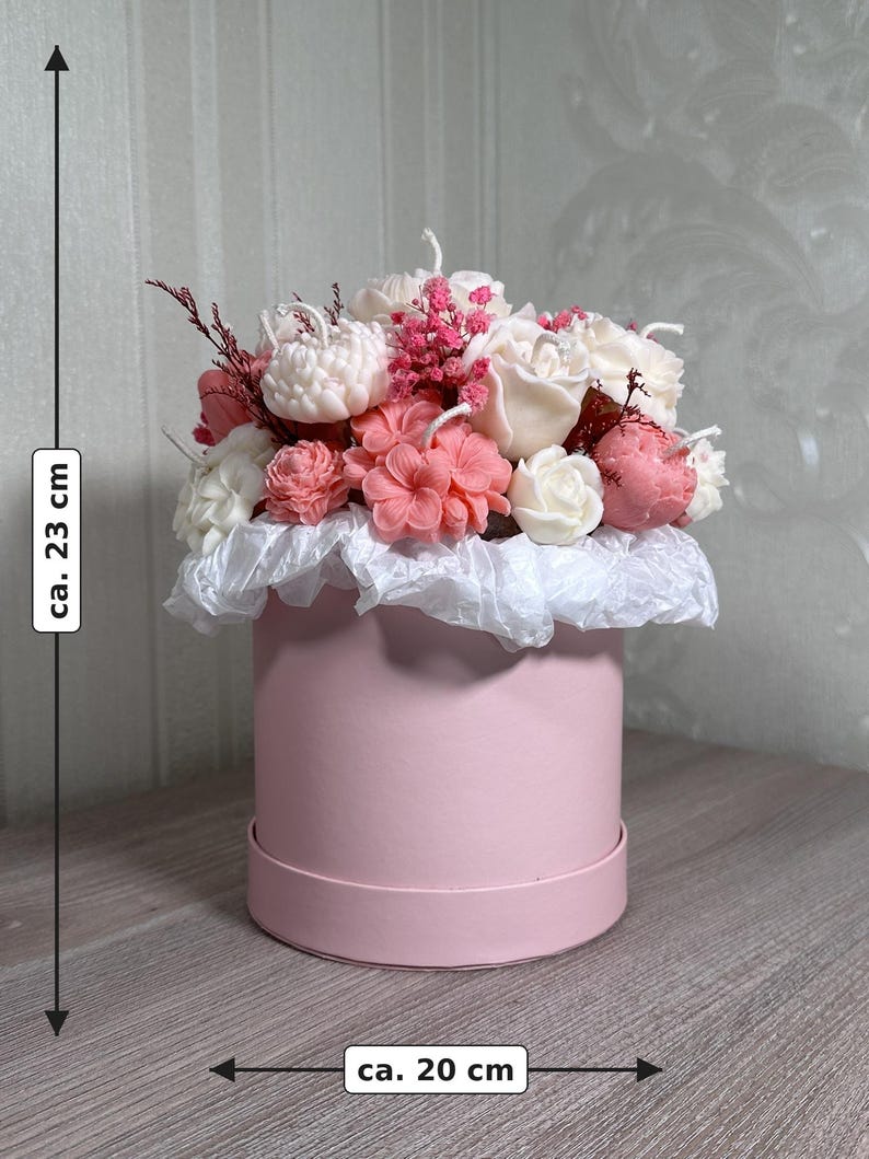 May include: A pink round gift box, approximately 8 inches in diameter and 9 inches tall, filled with a floral arrangement. The arrangement features white, pink, and red flowers, with a white paper ruffle around the base.