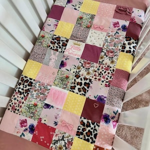 May include: A patchwork baby quilt in a cot, with squares of pink, yellow, and burgundy fabrics. Some squares have floral, leopard, and bunny prints. The text "Little Princess" is visible on one square.