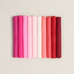 May include: A set of 12 rolled felt sheets in various shades of pink and red. The felt is arranged in a gradient from a deep burgundy to a light pink.