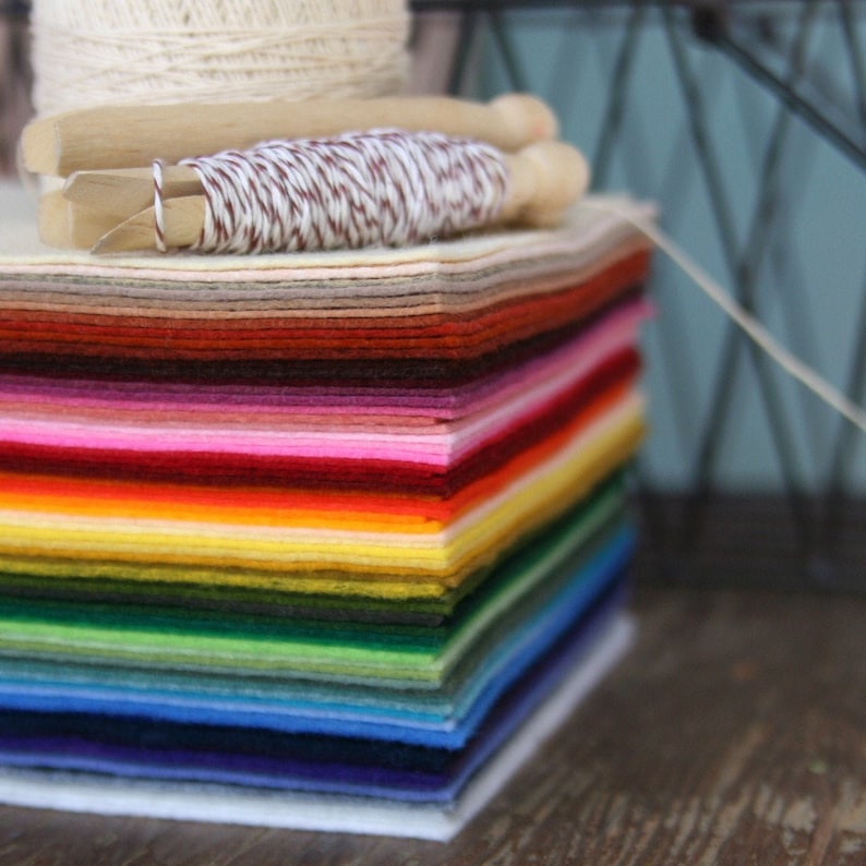 May include: A stack of colorful felt squares in various shades of red, orange, yellow, green, blue, purple, and white. The felt squares are arranged in a rainbow pattern.