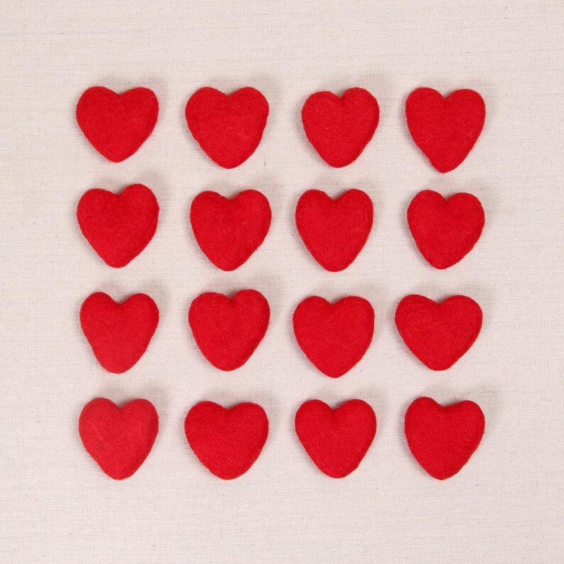 Puede incluir: Un conjunto de 16 corazones de fieltro rojo dispuestos en forma de cuadr&iacute;cula sobre un fondo de tela blanca.