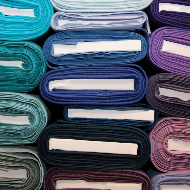 May include: A stack of fabric rolls in various shades of blue, purple, and teal. The fabric is folded neatly and has a smooth texture.