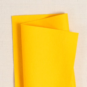 May include: A sheet of bright yellow felt fabric folded in half. The felt is smooth and has a soft texture.