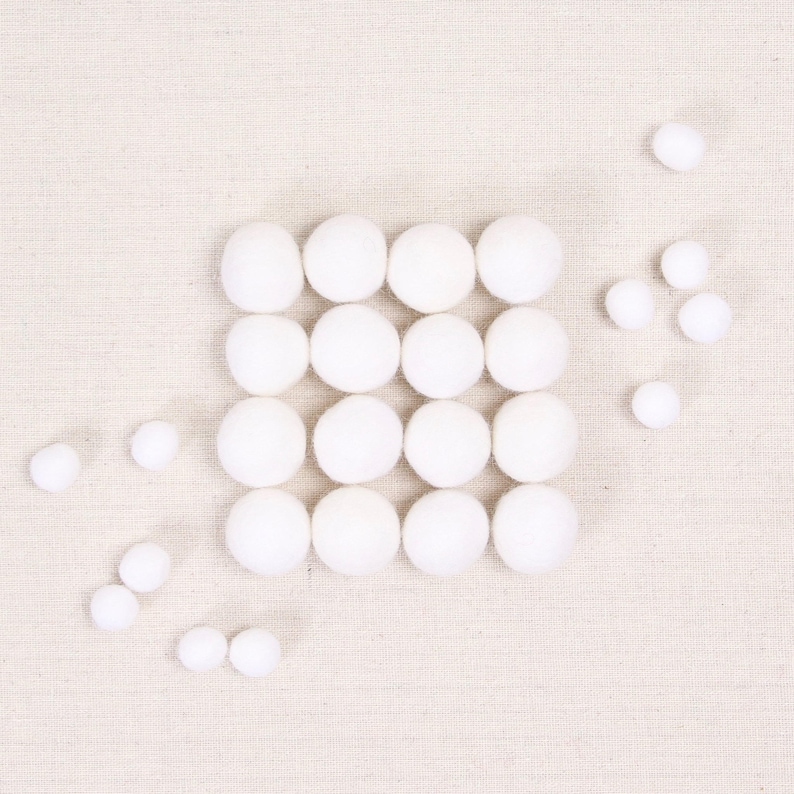 May include: A white felt ball garland with 25 white felt balls arranged in a square shape. There are additional white felt balls scattered around the square.