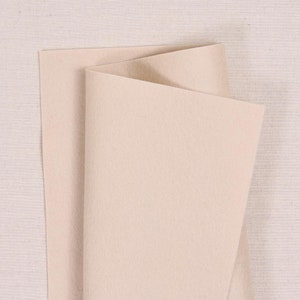 May include: A sheet of beige felt fabric folded in half. The felt is smooth and has a slightly textured surface.