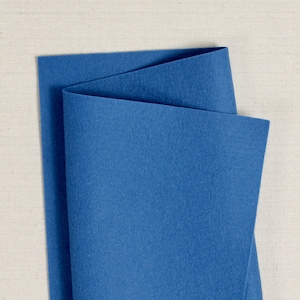 May include: A folded piece of blue felt fabric. The felt is a deep blue colour and has a smooth texture.