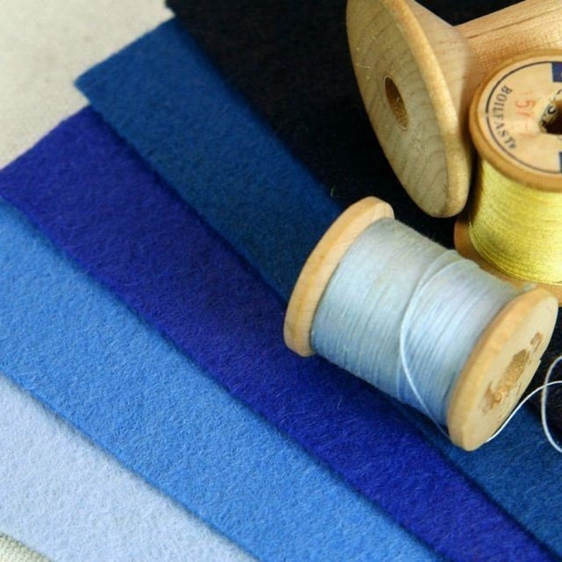 May include: A set of six fabric swatches in shades of blue, from light to dark, with two spools of thread, one light blue and one yellow.