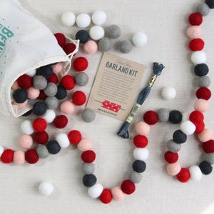 May include: A DIY garland kit with red, pink, white, and gray felt balls. The kit includes a bag of felt balls, a spool of thread, and instructions. The card reads "Garland Kit".