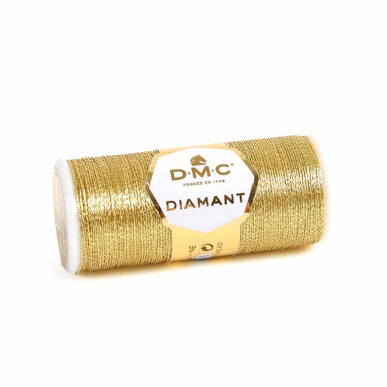 May include: A gold spool of DMC Diamant thread. The spool is labeled with the DMC logo and the text "DMC FOND&Eacute;E EN 1746 DIAMANT".