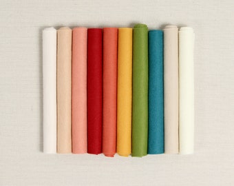 May include: A selection of rolled felt sheets in a range of colours, including cream, peach, red, coral, yellow, green, and teal. The felt rolls are arranged vertically against a neutral background, displaying the diverse colour palette.