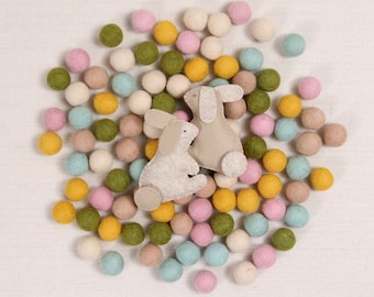 May include: Two felt bunny toys surrounded by a variety of colourful felt balls in pink, yellow, green, blue and white.