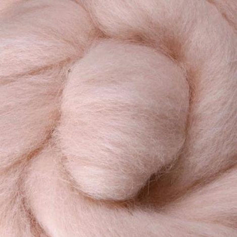 May include: A close-up of a soft, light pink wool roving. The wool is fluffy and textured, perfect for felting or spinning.