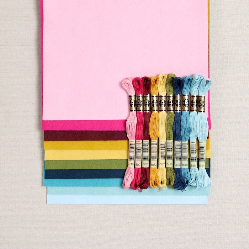May include: A set of 10 embroidery floss spools in various colors, including pink, red, yellow, green, blue, and light blue. The spools are arranged in a row on a stack of colorful felt squares.