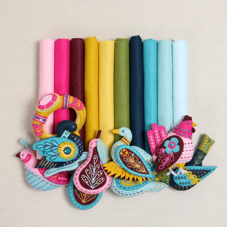 May include: A collection of felt ornaments featuring birds, a pear, and a wreath. The ornaments are decorated with colorful embroidery and beads. The ornaments are arranged on a background of colorful felt fabric.