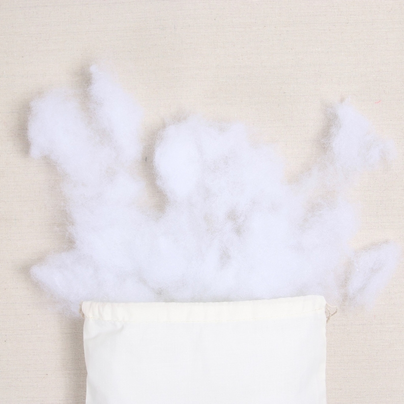 May include: White cotton stuffing spilling out of a white canvas bag. The bag is made of natural fabric and has a drawstring closure.