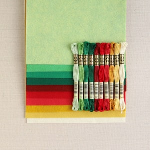 May include: A set of 12 embroidery floss spools in various colours, including green, red, yellow, and white. The spools are arranged in a row and are labelled with numbers.