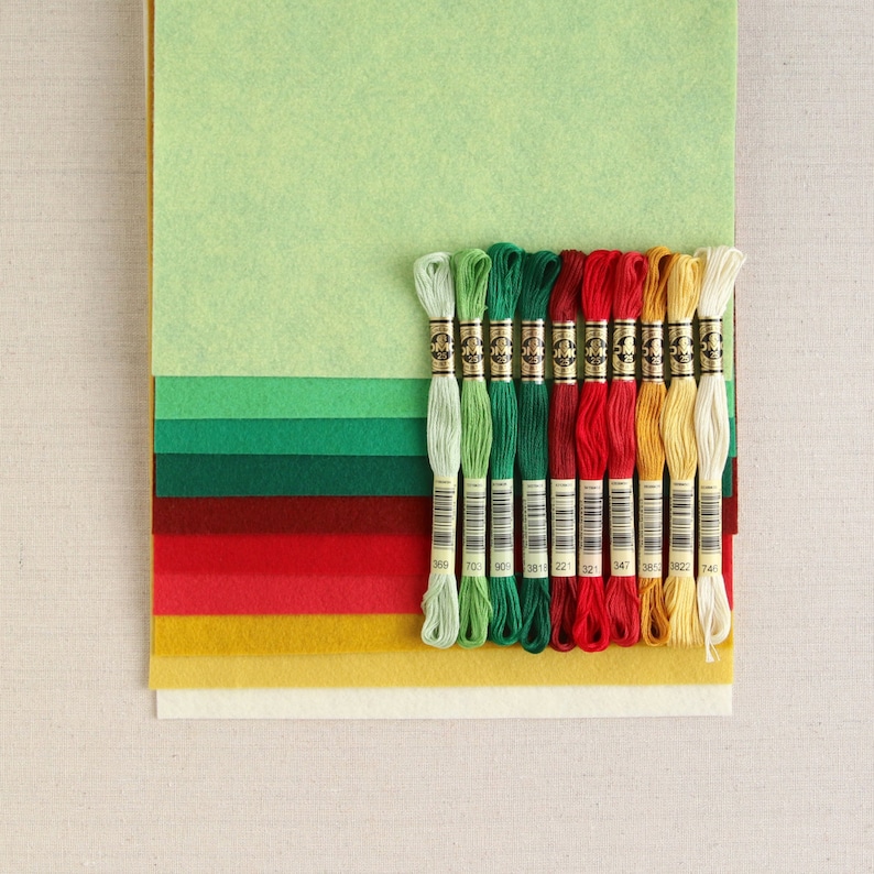 May include: A set of 12 embroidery floss spools in various colours, including green, red, yellow, and white. The spools are arranged in a row and are labelled with numbers.