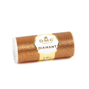 May include: A spool of gold metallic thread with the DMC Diamant label. The label is white with gold lettering and features the DMC logo, a horse's head.
