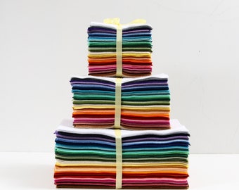 May include: Three stacks of colorful fabric squares, arranged in a tiered pyramid. Each stack is bound with a yellow ribbon. The fabric squares display a spectrum of colors, from deep reds and purples to vibrant greens and blues.