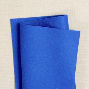 Puede incluir: Una hoja de fieltro azul brillante doblada por la mitad. El fieltro es liso y tiene una superficie ligeramente texturizada.