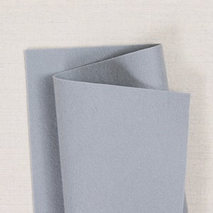 May include: A sheet of light gray felt fabric folded in half. The felt is smooth and has a slightly textured surface.