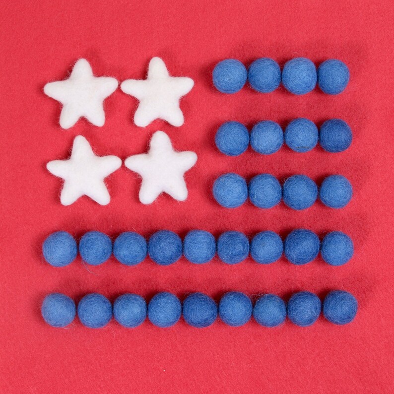 May include: A red felt background with a felt American flag design. The flag is made of white felt stars and blue felt circles.