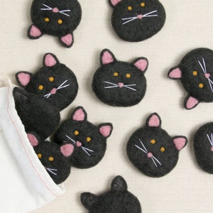 May include: A set of ten black felt cat toys with pink ears and white whiskers. The cats have yellow eyes and are arranged in a variety of positions.