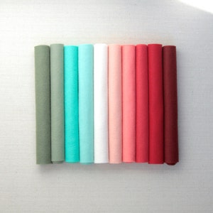 Puede incluir: Diez rollos de tela de fieltro en varios tonos de verde, azul, blanco, rosa y rojo. Los rollos est&aacute;n dispuestos en un degradado de verde a rojo.