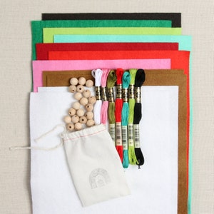 May include: A craft kit with felt squares in various colors, wooden beads, and embroidery floss. The kit includes a white felt square, a brown felt square, and a bag of wooden beads.