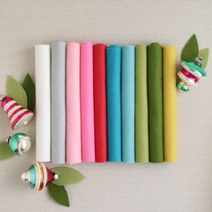 Könnte beinhalten: Sortiment aus zehn Filzplatten in verschiedenen Farben, darunter Weiß, Grau, Rosa, Rot, Türkis, Blau, Grün und Gelb. Die Filzplatten sind aufgerollt und in einer Reihe angeordnet.