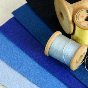 May include: A collection of six fabric swatches in shades of blue, ranging from light to dark, with two spools of thread, one light blue and one yellow, on top.