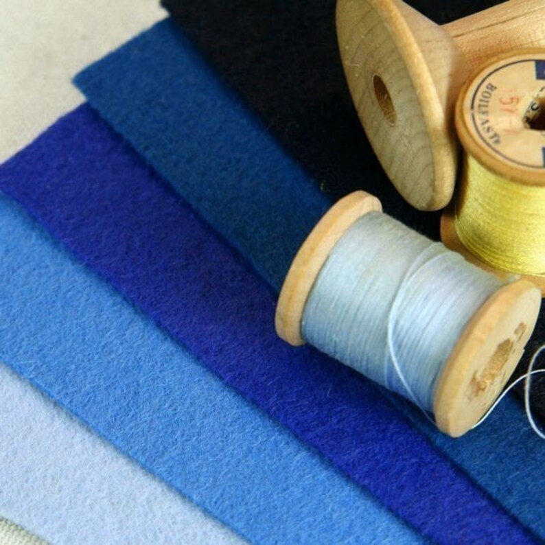 May include: A collection of six fabric swatches in shades of blue, ranging from light to dark, with two spools of thread, one light blue and one yellow, on top.