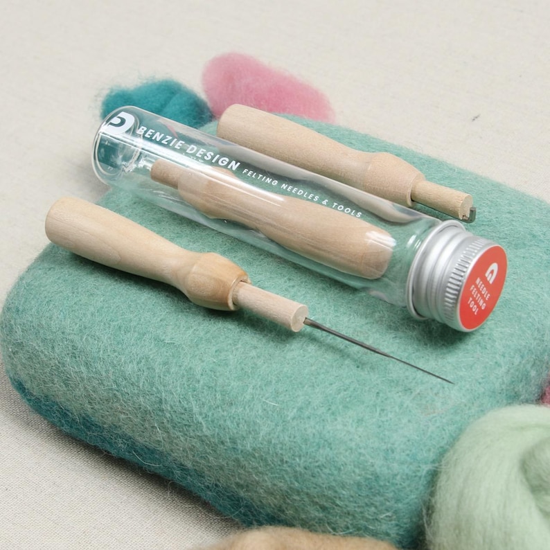 May include: A set of two felting needles in a clear glass tube with a silver lid. The needles have wooden handles and are used for needle felting. The tube has the text "Benzie Design Felting Needles & Tools" printed on it.