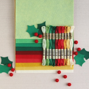 May include: A set of 12 embroidery floss spools in various colours, including red, green, and yellow. The spools are arranged in a row on a multi-coloured felt background with holly leaf cutouts.