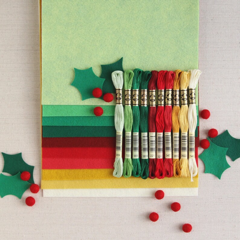 May include: A set of 12 embroidery floss spools in various colours, including red, green, and yellow. The spools are arranged in a row on a multi-coloured felt background with holly leaf cutouts.