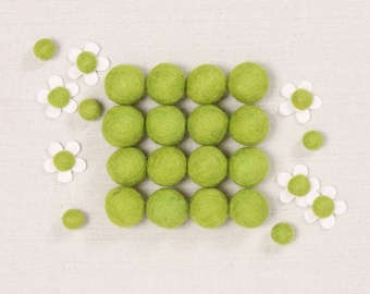 Könnte beinhalten: Eine quadratische Anordnung von 25 grünen Filzkugeln auf einem weißen Leinenhintergrund. Die Kugeln sind von weißen Filzblumen mit gelben Zentren umgeben.